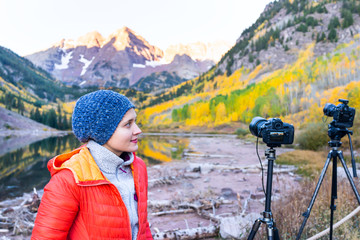 Fototapeta na wymiar Maroon Bells lake in Aspen, Colorado in autumn at sunrise with woman cold with hat standing by cameras on tripods