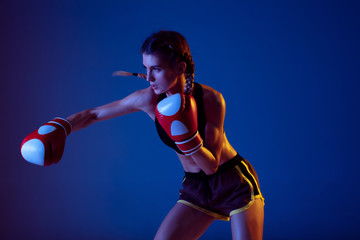 Target. Fit caucasian woman in sportswear boxing on blue studio background in neon light. Novice...