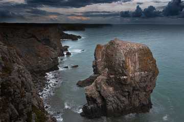 Fototapeta na wymiar Sunrise at stack rocks, on dramatic coast of Pembrokeshire, South Wales, Uk.Moody sky at dawn over coastline with rocky cliffs , coastal feature and turquoise sea water.Majestic seascape. 