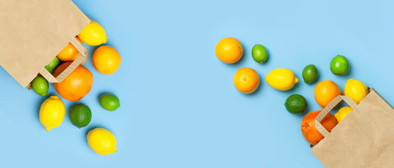 Creative background with tropical fruits. Orange, lemon, lime, grapefruit drop out of paper bag on blue background. Flat lay top view copy space. Food concept, vitamin C, disease prevention, flu