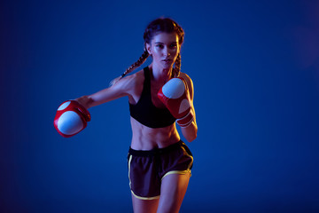 Beauty. Fit caucasian woman in sportswear boxing on blue studio background in neon light. Novice...