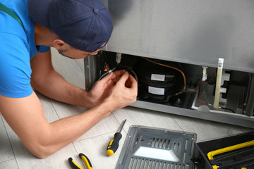 Professional male technician repairing broken refrigerator indoors