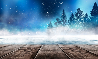 Winter background. Winter snow landscape with wooden table in front. Dark winter forest background at night. Snow, fog, moonlight. Dark neon night background in the forest with moonlight. 
