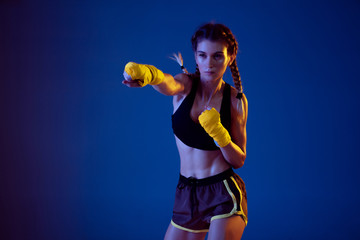 Sunshine. Fit caucasian woman in sportswear boxing on blue studio background in neon light. Novice...