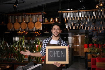 Young business owner holding sign OPEN in his cafe