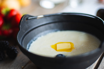 Traditional breakfast milk porridge with butter and berries on a wooden table.