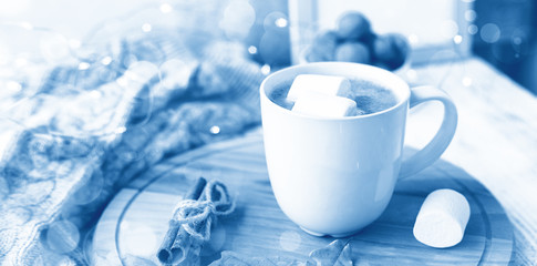 Mug of coffee with marshmallow, knitted scarf, garland. Hygge concept. Soft focus. Toned classic blue trend color