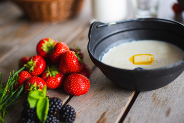 Traditional breakfast milk porridge with butter and berries on a wooden table.