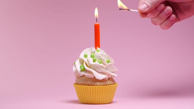 Woman lighting birthday candle on pink background, closeup