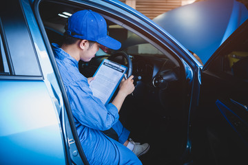 Mechanic holding clipboard and checking inside car to maintenance vehicle by customer claim order in auto repair shop garage. Repair service. People occupation and business job. Automobile technician