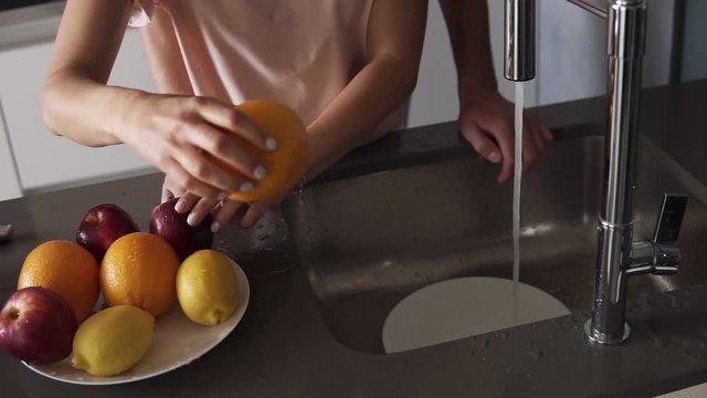 Unrecognizable loving couple wash fresh fruits in sink before eating in the morning on the modern kitchen. Man in jeans gently stroking the back of his caring wife