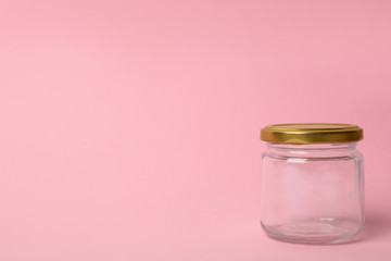 Closed empty glass jar on pink background, space for text