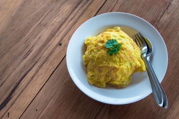 Thai fried egg or Omelet with rice underneath placed on wooden table