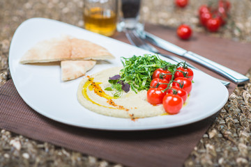 Traditional appetizer hummus with bread cakes, pita, on a plate with vegetables and sauce.