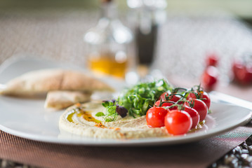 Traditional appetizer hummus with bread cakes, pita, on a plate with vegetables and sauce.