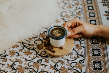 Closeup of woman's hand holding espresso cup on floral pattern