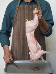 man’s hands carve raw rabbit meat into pieces