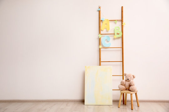 Teddy bear on chair and decorative ladder near wall in child room. Space for text