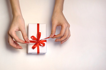 female hands pull a red ribbon on a gift box on a light background. Christmas and New Year or season greetings. Selective focus
