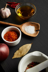 Spices, chili peppers with salt on wooden spoon and olive oil on black wooden background