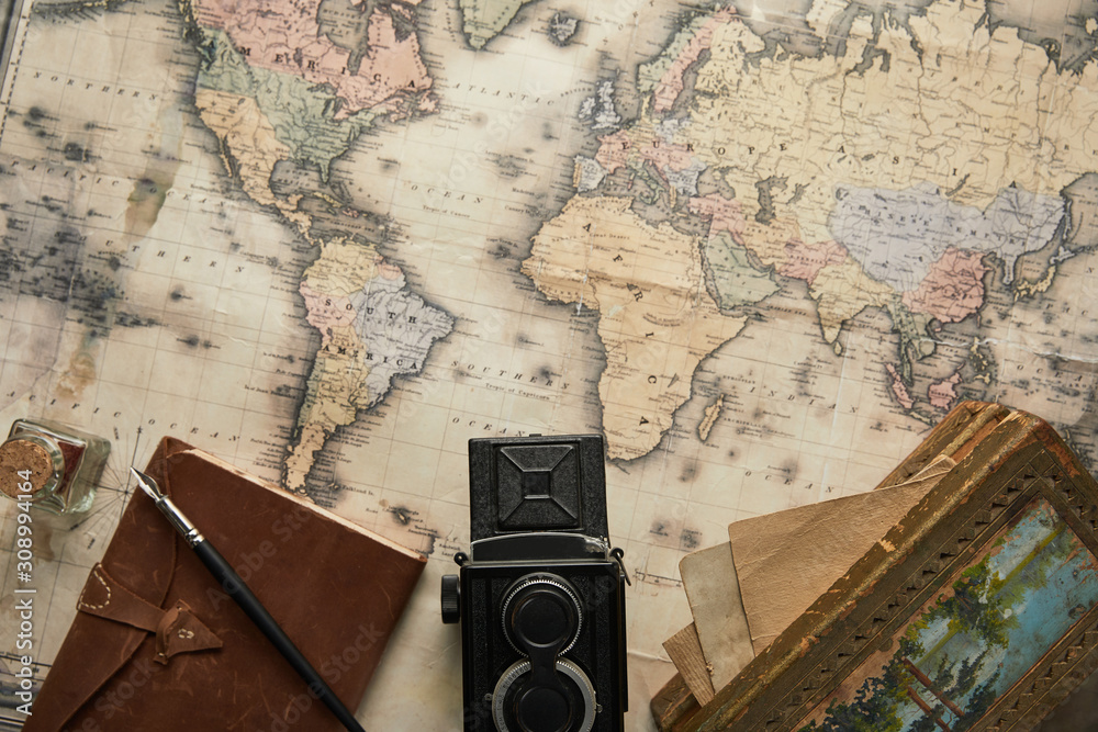 Wall mural top view of vintage camera, notepad with fountain pen and painting on map background