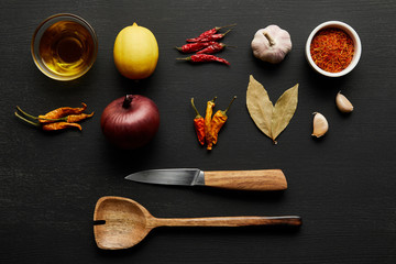 Top view of spices, olive oil with lemon and onion on black wooden background