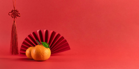 Two fresh tangerines, Chinese knot and red fan on fiery red background. Chinese new year traditions. Banner design, template greeting card, space for text