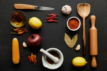 Top view of wooden kitchenware with ripe vegetables and spices on black wooden background