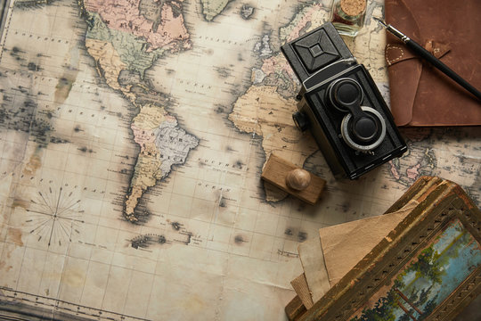 top view of vintage camera, notepad with fountain pen, stamp and painting on map background