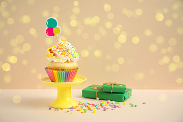 Birthday cupcake and gift boxes on beige background. Bokeh effect
