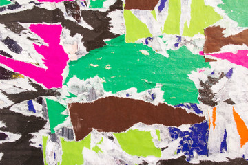 Torn and ripped colorful pieces of old shabby gloss paper placards on dirty billboard texture...