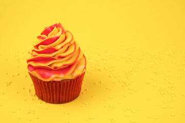 Cupcake on birthday with red and yellow cream on yellow background, decorated with sprinkles.