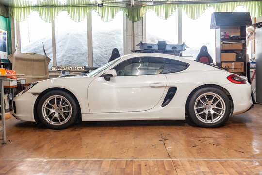 Side View Of Luxury Very Expensive New White Porsche Cayman Coupe Sportcar Stands In The Detailing Box Waiting For Repair In Auto Service