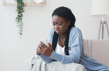 Young black woman looking at smartphone screen with sad face expression, free space