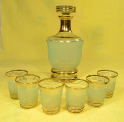 On the table on a uniform yellow background is a green with a gold ring glass decanter and a group of stacks.