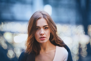 Attractive charming young woman in the holiday park. Blue trendy color ackground. Blurry lights. The holiday mood.