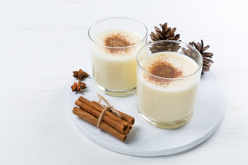 Eggnog with cinnamon in glasses on wooden background, Christmas decor, traditional festive drink.