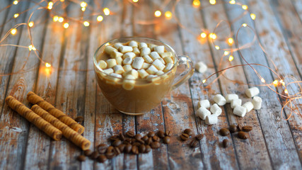 cocoa, marshmallows, homemade cookies and heart made from coffee beans on wooden background with bokeh New Year's lights.