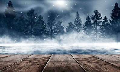 Winter background. Winter snow landscape with wooden table in front. Dark winter forest background at night. Snow, fog, moonlight. Dark neon night background in the forest with moonlight.