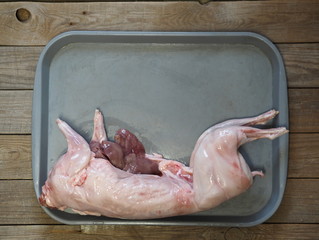 carcass of raw rabbit meat on a gray tray on a wooden rustic table