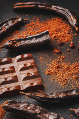 Carob chocolate and carob fruit powder on dark background. A tasty and useful substitute for chocolate.