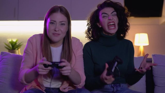 Female friends playing video game with joysticks, victory and loss emotions