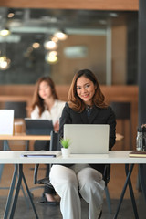 Confidently young businesswoman looking at the camera and sitting on modern office workplace.