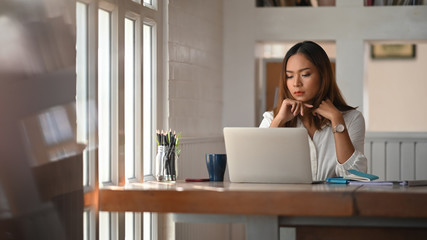 Asian woman working on home office table with thinking moment on laptop.