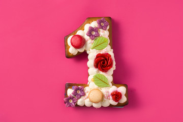 Number one cake decorated with flowers and cookies on pink background. 