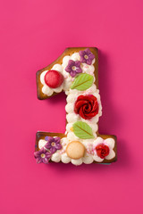 Number one cake decorated with flowers and cookies on pink background.
