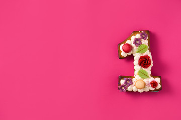 Number one cake decorated with flowers and cookies on pink background. Copy space	