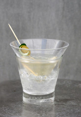 Glass of clear alcoholic drink with olive, lime peel and ice cubes.Close-up of glass with ice cubes, olive and lime
