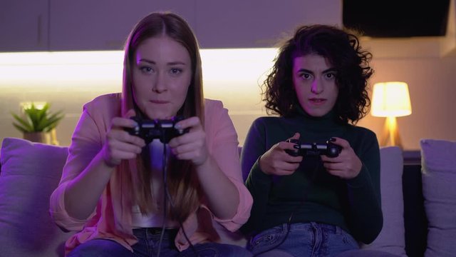 Excited young women playing video game home together, enjoying evening leisure