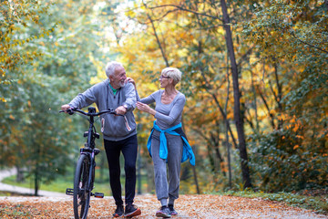 Mature couple woman and man with bicycle walking in the park and talk
